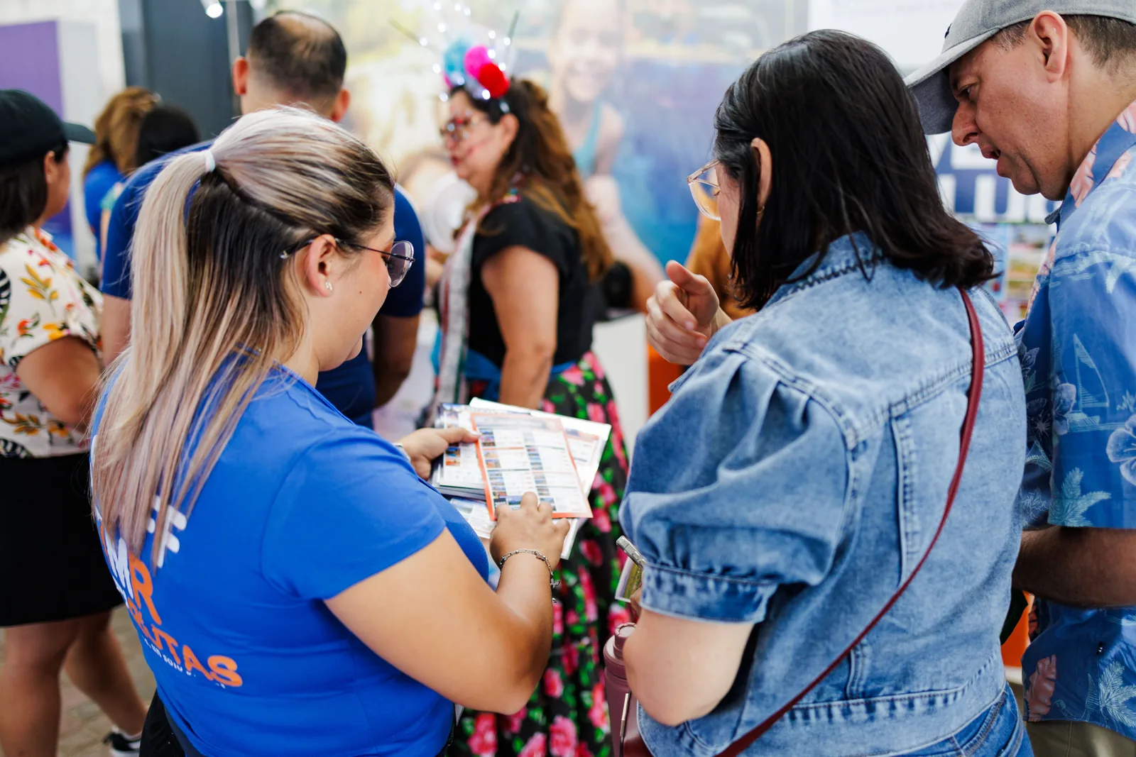 Asesora de una agencia mostrando folletos de viaje a dos visitantes en su stand