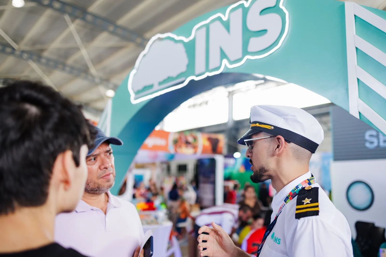Visitantes conversando con un oficial de cruceros uniformado en un stand del evento